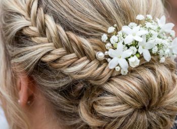 Peinado de novia con trenza lateral y adornos de flores blancas en el recogido.