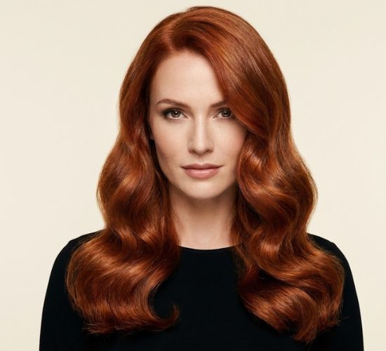 Mujer con cabello rojo brillante y ondas sueltas, vestida de negro.