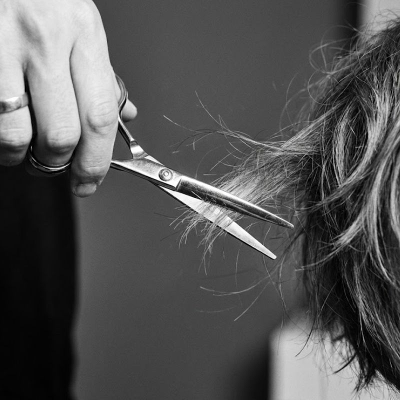 Mano cortando pelo con tijeras en un salón de belleza.