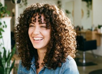 Mujer con cabello rizado sonriendo en un salón de belleza luminoso